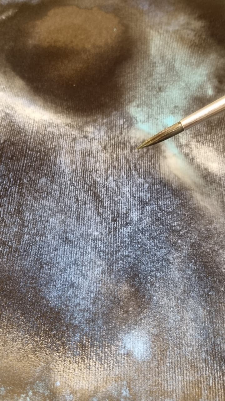Pincel aplicando acuarela metálica sobre fondo oscuro